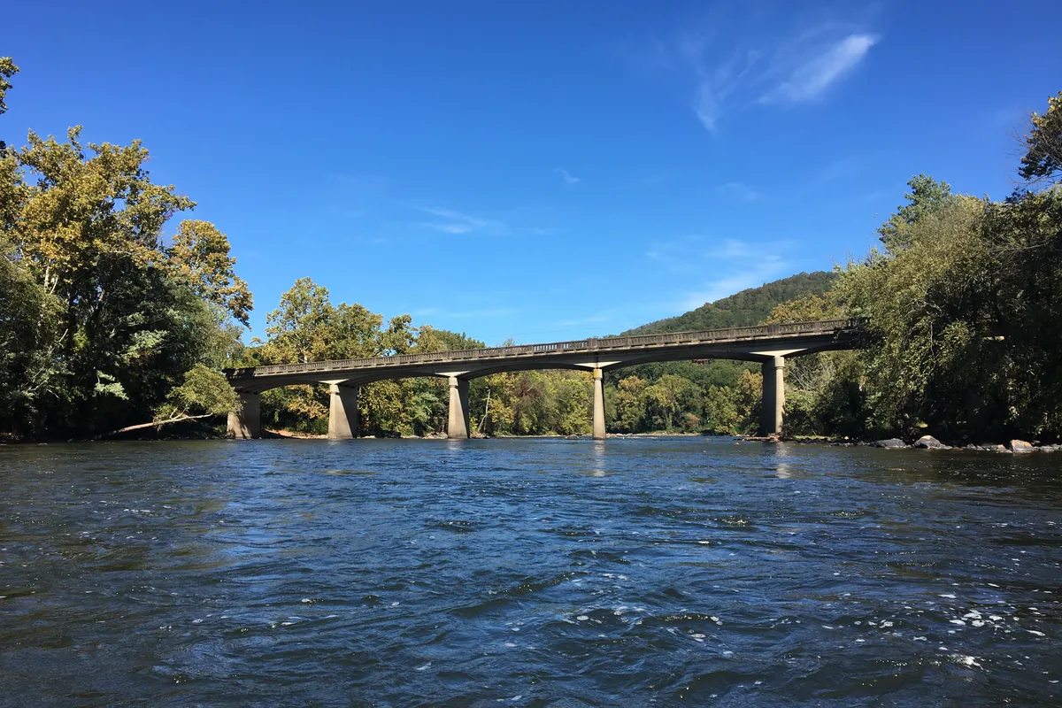 The French Broad River running between wooded ridges in Madison County, North Carolina, with a highway bridge crossing downstream