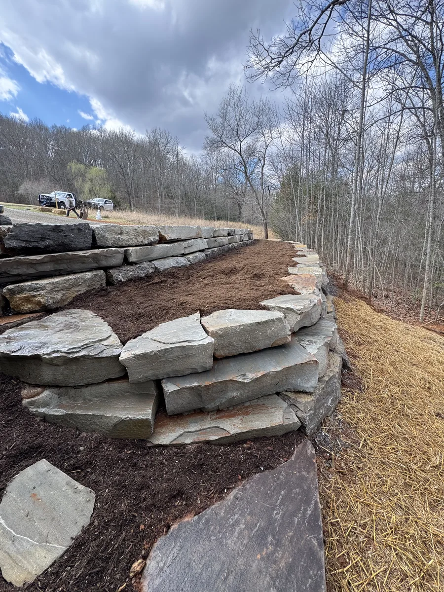 Layered flat boulders forming a low wall along a sloped grassy area