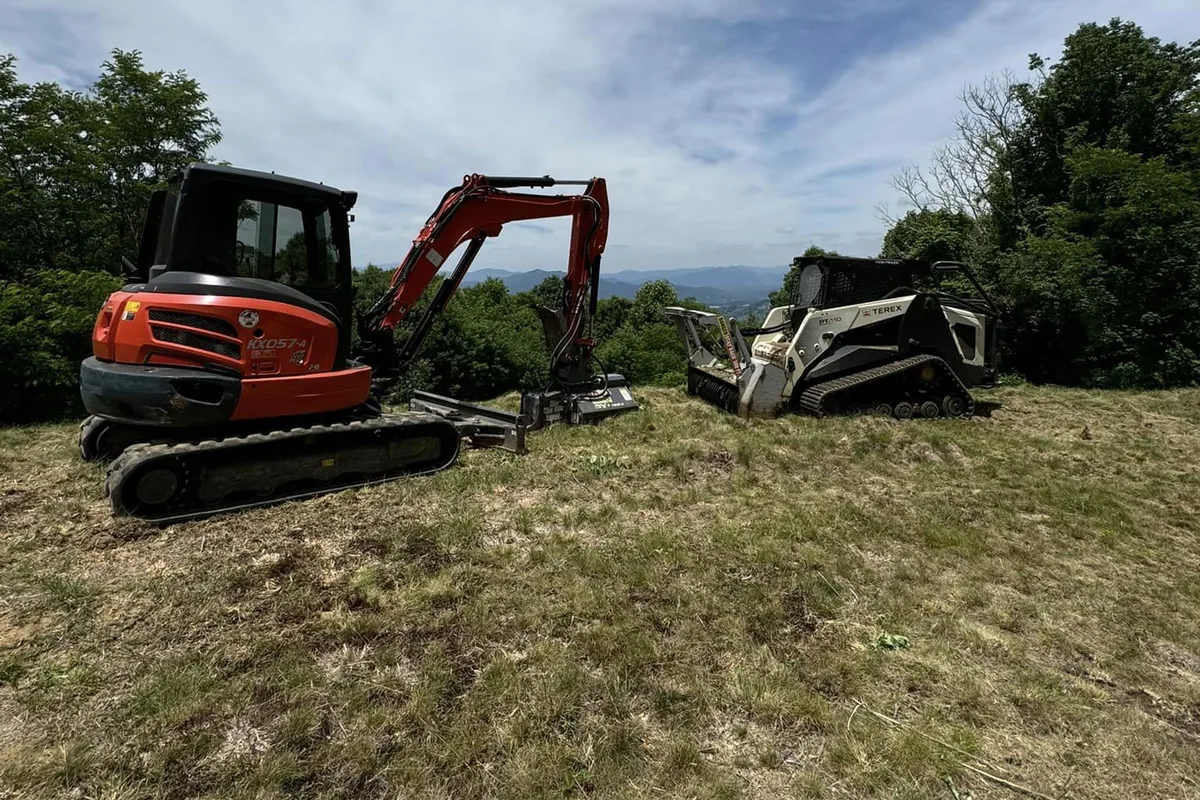 Excavator and tracked machine parked on open hilltop ground with mountains in the distance
